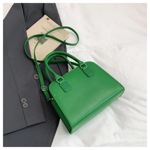 Top view of green leather Boston bag on white fabric with fashion magazine backdrop