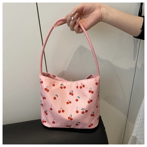 Detail showing pink tote bag with cherry print and slender handles in a hand-held view