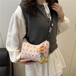 Pink pleated crossbody bag with polka dots and flower charm, shown on model in soft lighting