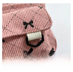 Detail of pink corduroy backpack featuring black bow patterns and durable strap hardware