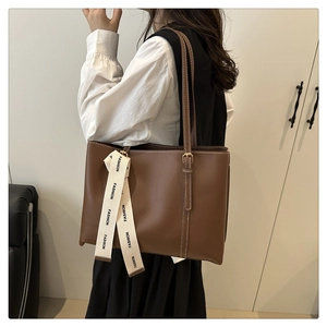 Dettaglio laterale di una borsa tote in pelle marrone con nastro decorativo FASHION