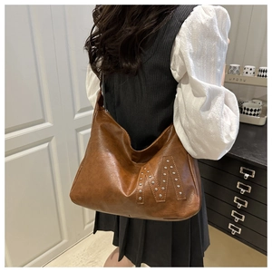 Close-up of a brown leather tote bag featuring a silver rivet M logo and vintage design