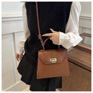 Detail of caramel brown crossbody bag with gold metal buckle and top handle worn by model