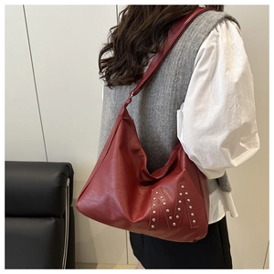 Detail of dark red leather tote bag with silver rivet M design worn by a model