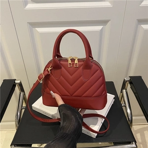 Red quilted shell bag with elegant V-stitching and gold hardware on a white art book