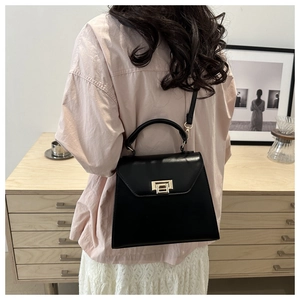 Rear view of a model wearing a black trapezoidal leather bag with gold metal clasp