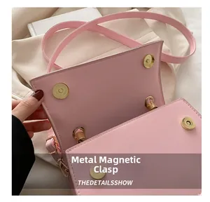 Detail of golden magnetic hardware buckles on a textured pink square shoulder bag