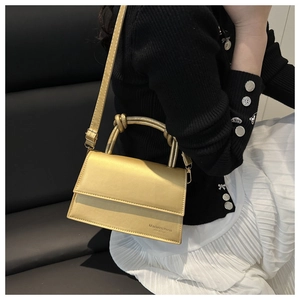 Detail of metallic gold square handbag with mini & bags embossing and circular handle