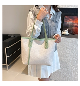 Detail of white leather tote with green straps featuring embossed floral and text patterns