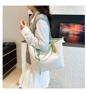 Detail of white leather tote bag with green trim and embossed heart patterns on model