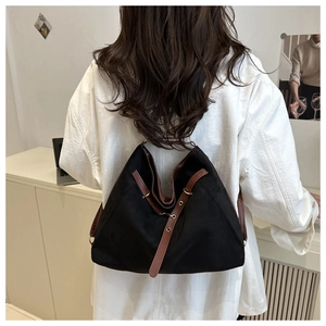 Detail of a large black tote bag with brown leather straps and vintage eyelet accents