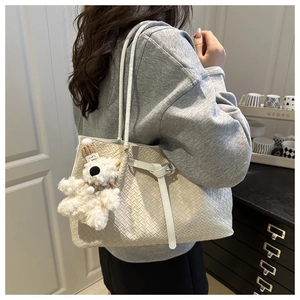 Détail d'un sac cabas tressé blanc avec sangles et un joli pendentif ours en peluche