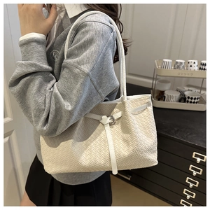 Détail d'un cabas tressé crème avec lanières en cuir blanc et boucles métalliques