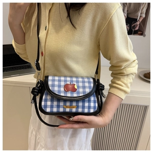 Detail of blue plaid crossbody bag featuring red apple motif and knotted shoulder strap