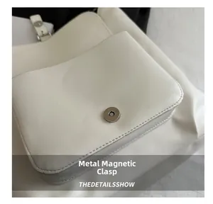Detail of silver magnetic buckle closure and soft white leather texture on handbag