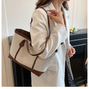 Side view of beige canvas tote bag with brown leather handles worn by a model