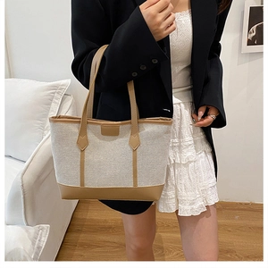 Detail view of contrast canvas tote bag with brown leather trim held by a model
