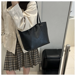 Detail shot of black leather tote bag featuring long shoulder straps and debossed brand logo