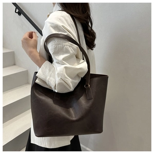 Detail of dark brown leather tote bag with dual shoulder straps worn by a model