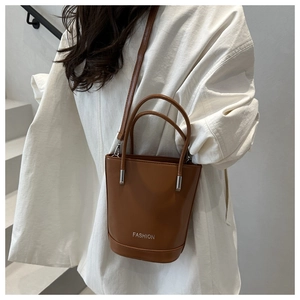 Detailed view of brown leather bucket bag featuring silver Fashion logo and metal handle