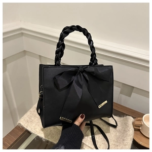 Detail of black handbag featuring a large satin bow and woven leather handle accents