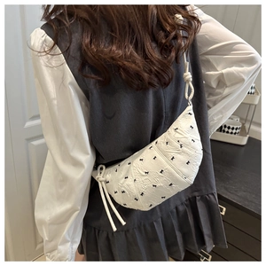 Detail of white pleated dumpling bag featuring black bow patterns and knotted strap