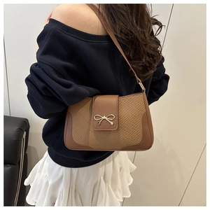 Detail of caramel brown underarm bag with gold bow clasp and woven leather texture