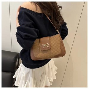 Detail of a brown leather woven shoulder bag with a gold bow buckle on a model