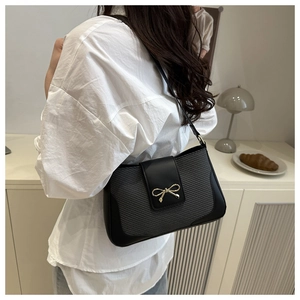 Detail of minimalist black leather shoulder bag with gold bow clasp on a female model