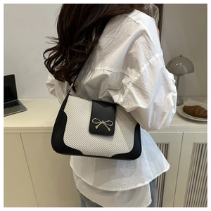 Detail of white woven underarm bag with black trim and golden bow clasp on a model