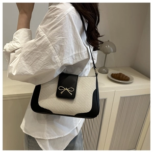 Detail of a chic black and white woven underarm bag with gold bow clasp on a model