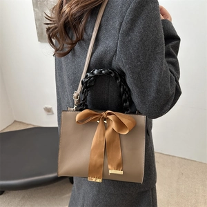 Brown leather square handbag with large satin bow and woven handle on grey blazer model