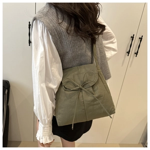 Olive green nylon crossbody tote with bow detail on a casual white shirt and grey vest