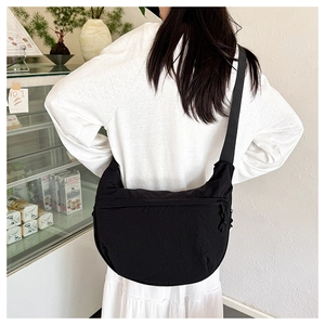 Rear view of a black nylon crescent crossbody bag worn by a model in a cozy cafe