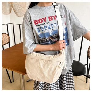 Detailed shot of cream nylon crossbody bag with wide strap and side knot zipper detail