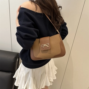 Elegant woven shoulder bag in brown leather with a golden bow buckle shown on a model