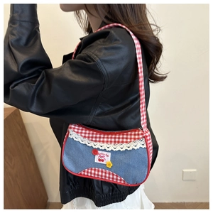 Detail of red plaid and denim shoulder bag with lace trim and cherry patch on model