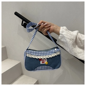 Detail of red cherry patch and lace trim on a blue denim plaid crossbody bag