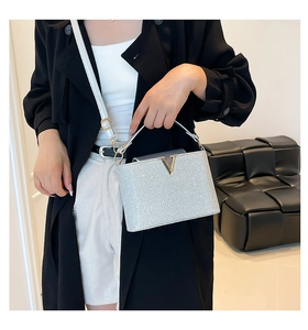 Detail of silver glitter handbag with gold V-logo and white adjustable strap on a model