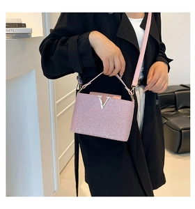 Détail d'un sac à main rose à paillettes avec logo en V métallique et poignée en cuir