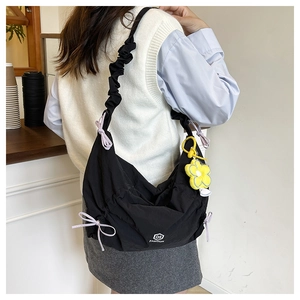 Detail of black pleated shoulder bag with purple ribbons and yellow flower charm
