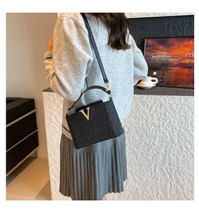 Détail de la texture noire scintillante et du logo V doré sur le petit sac à main