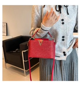 Vue détaillée du sac à main rouge scintillant avec boucle dorée en V porté par un mannequin