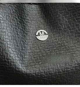 Macro shot of black lychee grain leather with silver 'M FASHION' metal logo plaque
