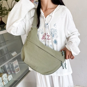 Sage green nylon half-moon crossbody bag shown on a model in a minimalist outdoor setting