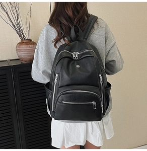 Detailed back view of a black lychee texture backpack worn by a model in a stylish room