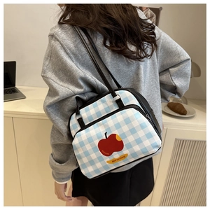 Detail of blue plaid shoulder bag with red apple print and black leather straps