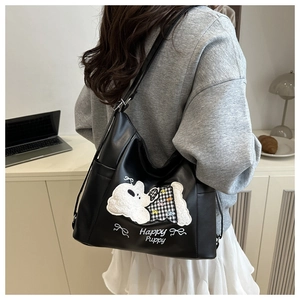 Close-up of black leather tote bag with Happy Puppy embroidery and plush puppy patch