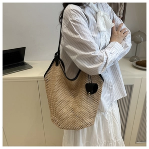 Detail of hand-woven straw tote bag featuring black faux leather straps and a tassel charm