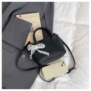 Close-up of black lychee leather mini tote bag with pearl lace bow charm on white fabric